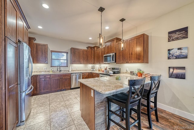 kitchen featuring a breakfast bar, decorative light fixtures, light stone counters, kitchen peninsula, and stainless steel appliances