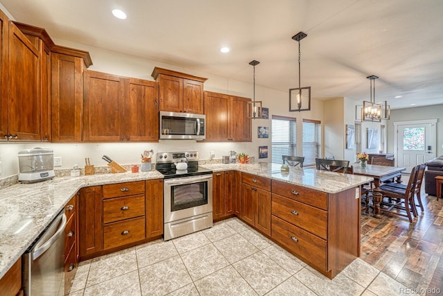 kitchen featuring appliances with stainless steel finishes, pendant lighting, light tile patterned floors, light stone counters, and kitchen peninsula