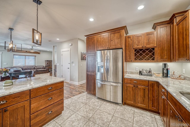 kitchen with pendant lighting, light tile patterned floors, light stone counters, and stainless steel fridge