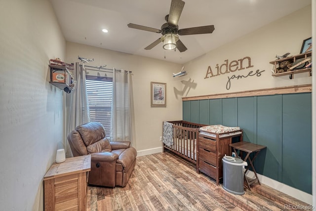 bedroom featuring hardwood / wood-style flooring, a crib, and ceiling fan