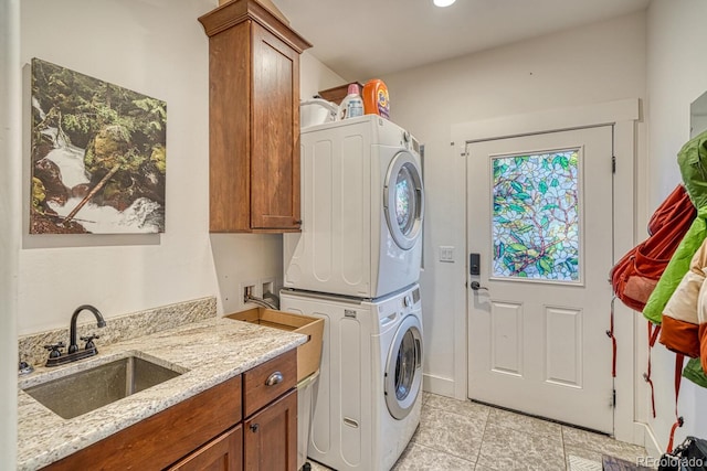 laundry area featuring sink, light tile patterned flooring, cabinets, and stacked washing maching and dryer