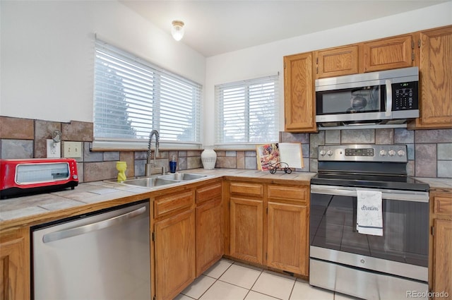 kitchen with appliances with stainless steel finishes, tasteful backsplash, sink, light tile patterned floors, and tile counters