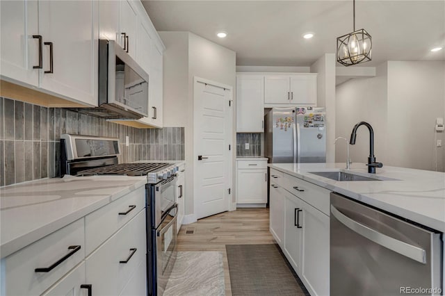 9836 Banner Peak St, Littleton, CO 80125 - kitchen featuring appliances with stainless steel finishes, a sink, white cabinetry, hanging light fixtures, and light stone countertops