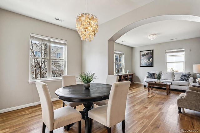 dining area with arched walkways, light wood-type flooring, visible vents, and baseboards