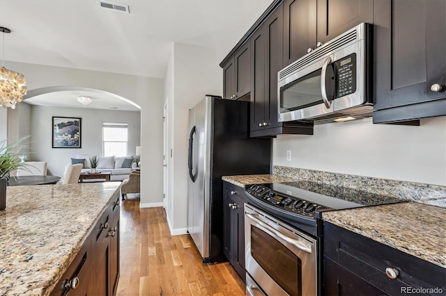 kitchen with arched walkways, stainless steel appliances, visible vents, open floor plan, and light wood finished floors