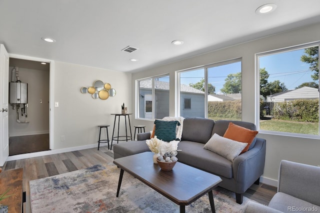 living room featuring baseboards, water heater, visible vents, and wood finished floors