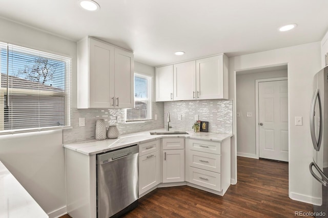 kitchen with stainless steel appliances, a sink, white cabinets, light stone countertops, and dark wood-style floors