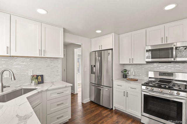 kitchen featuring dark wood-style flooring, stainless steel appliances, white cabinets, a sink, and light stone countertops