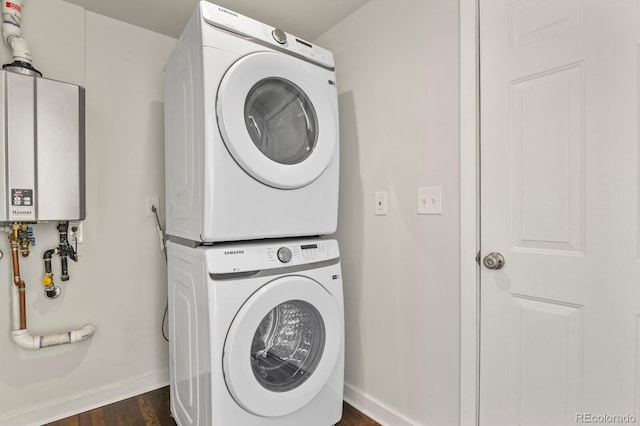 clothes washing area featuring stacked washer and dryer, water heater, dark wood-type flooring, laundry area, and baseboards