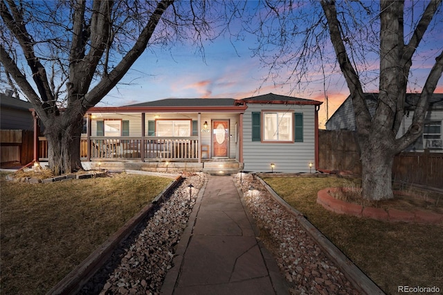 view of front of property featuring covered porch, a lawn, and fence