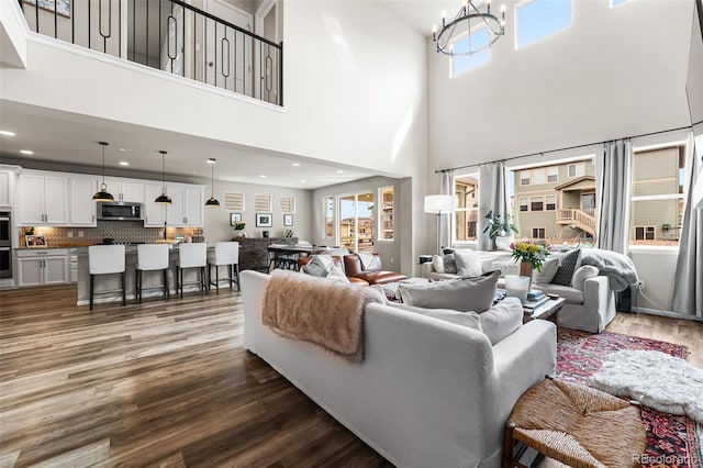 living area with an inviting chandelier, a towering ceiling, recessed lighting, and wood finished floors