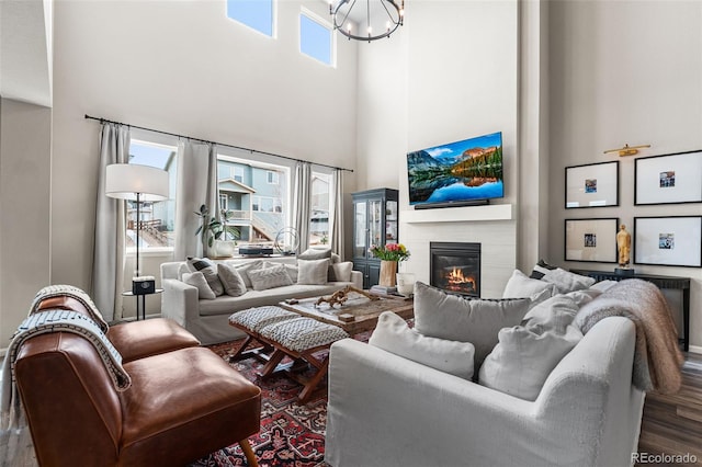 living room featuring a chandelier, wood finished floors, a towering ceiling, and a glass covered fireplace