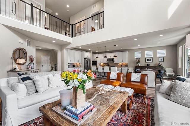 living area with a towering ceiling, wood finished floors, visible vents, and recessed lighting