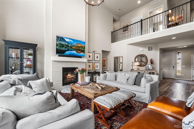 living room featuring a tile fireplace, visible vents, wood finished floors, and a high ceiling