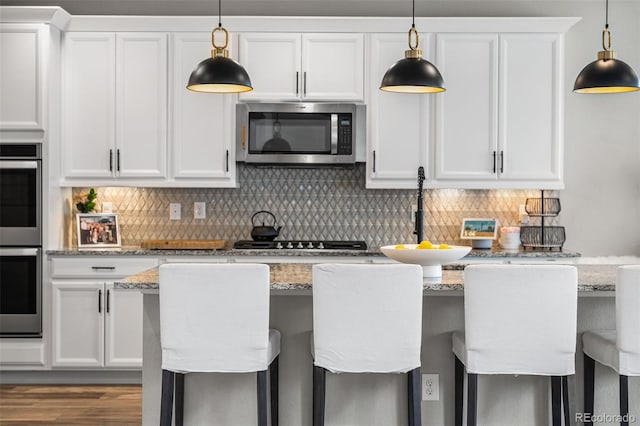 kitchen featuring white cabinets, appliances with stainless steel finishes, tasteful backsplash, and decorative light fixtures