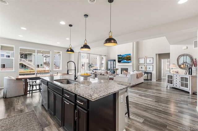 kitchen featuring a sink, light stone counters, dark wood finished floors, dishwasher, and dark cabinetry