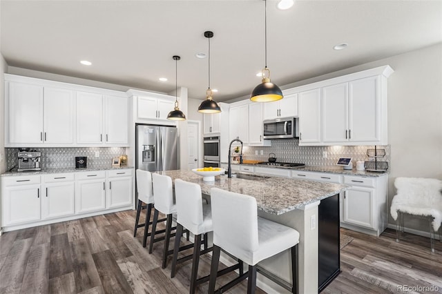 kitchen featuring dark wood-style flooring, a sink, decorative backsplash, a kitchen island with sink, and appliances with stainless steel finishes