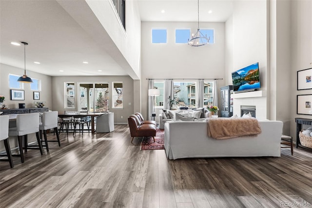 living area featuring wood finished floors, a fireplace, a notable chandelier, visible vents, and a towering ceiling