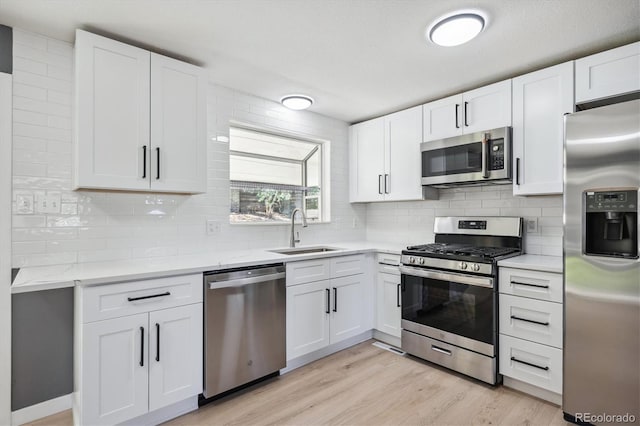 kitchen with appliances with stainless steel finishes, sink, white cabinets, and light hardwood / wood-style floors