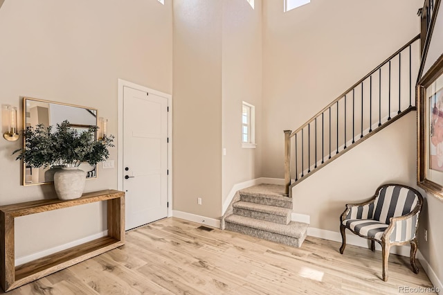 entrance foyer featuring a towering ceiling, baseboards, stairway, and light wood-style flooring