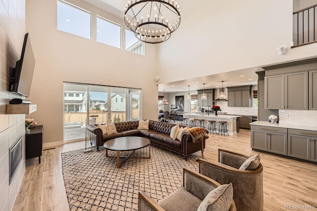 living room featuring light wood-style flooring, a high ceiling, a chandelier, healthy amount of natural light, and recessed lighting