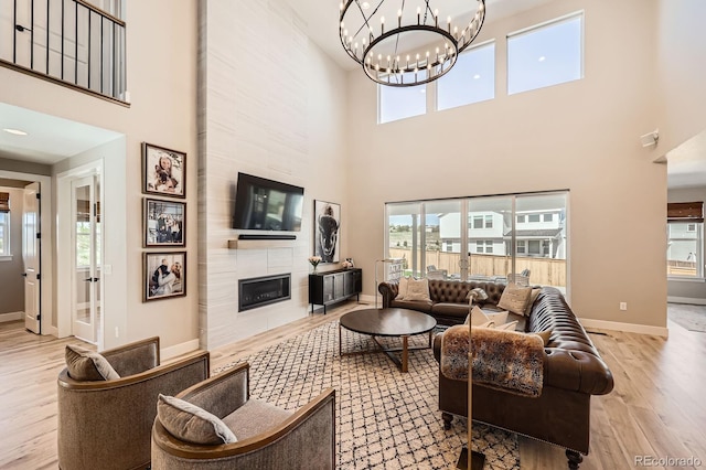 living area with wood finished floors, a tiled fireplace, a towering ceiling, baseboards, and a chandelier