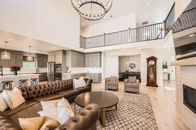 living room featuring a chandelier, a high ceiling, light wood-style flooring, a fireplace, and recessed lighting