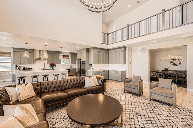 living room featuring a chandelier, light wood-type flooring, healthy amount of natural light, recessed lighting, and a towering ceiling