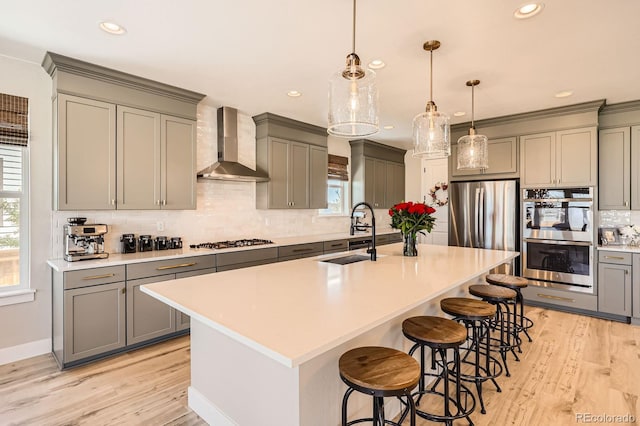 kitchen with a sink, appliances with stainless steel finishes, wall chimney exhaust hood, gray cabinetry, and decorative backsplash