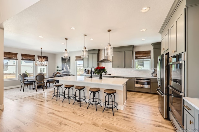 kitchen featuring appliances with stainless steel finishes, a breakfast bar area, light countertops, wall chimney range hood, and recessed lighting