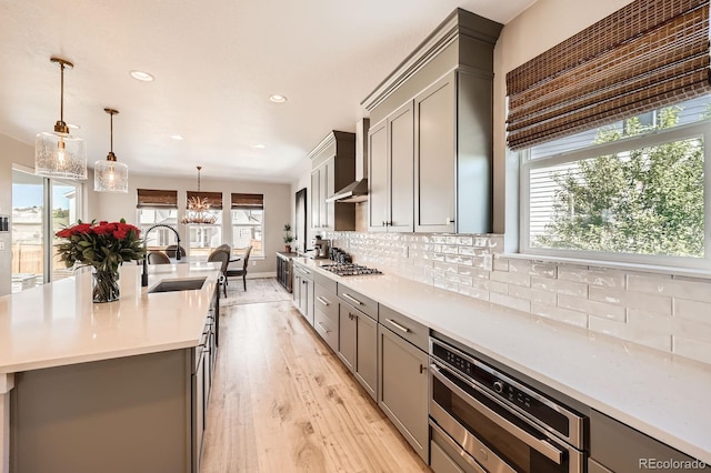 kitchen featuring a sink, gray cabinets, stainless steel appliances, light wood-type flooring, and wall chimney range hood