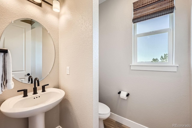 bathroom with a sink, toilet, wood finished floors, baseboards, and a textured wall