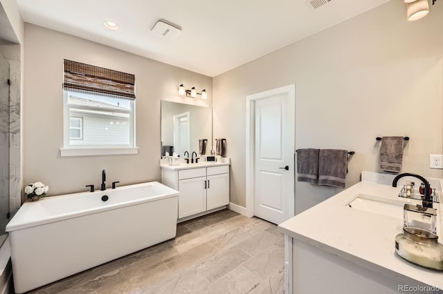 full bathroom featuring marble finish floors, two vanities, a freestanding tub, and recessed lighting