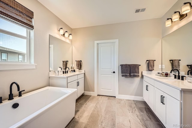 bathroom with two vanities, a freestanding tub, baseboards, and stone finish floors