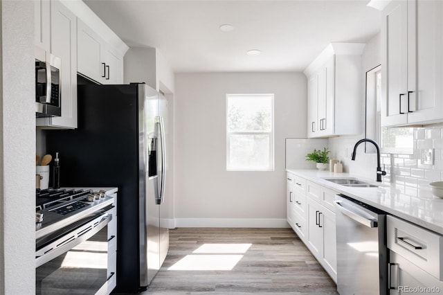 kitchen with appliances with stainless steel finishes, sink, backsplash, light hardwood / wood-style floors, and white cabinetry