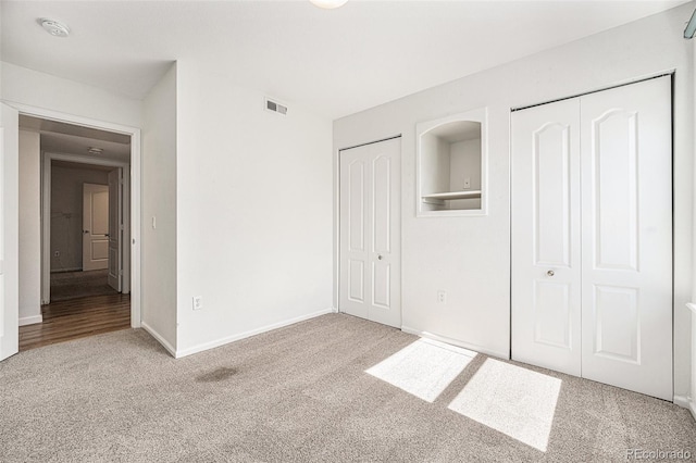 unfurnished bedroom with multiple closets and light carpet