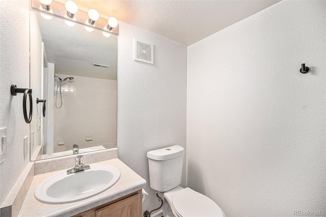 bathroom with vanity, tiled shower, a textured ceiling, and toilet