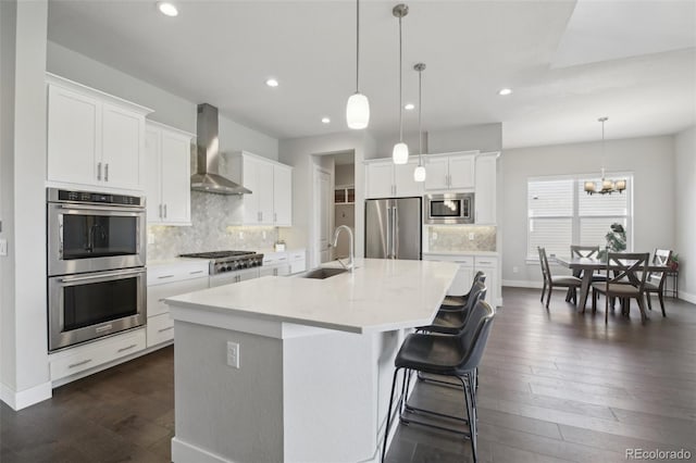 8803 Antero Ct, Arvada, CO 80007 - kitchen featuring stainless steel appliances, wall chimney range hood, a sink, a large island with sink, and decorative backsplash
