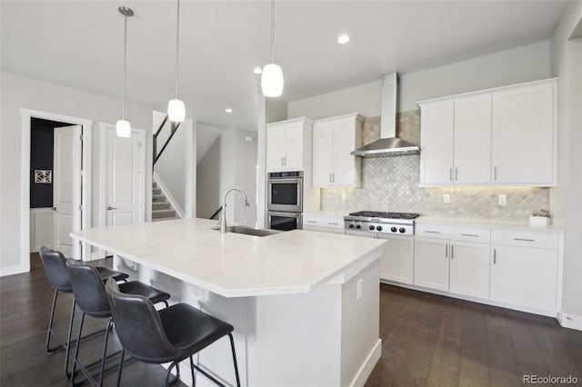 8803 Antero Ct, Arvada, CO 80007 - kitchen featuring wall chimney range hood, stainless steel appliances, a sink, tasteful backsplash, and a kitchen island with sink