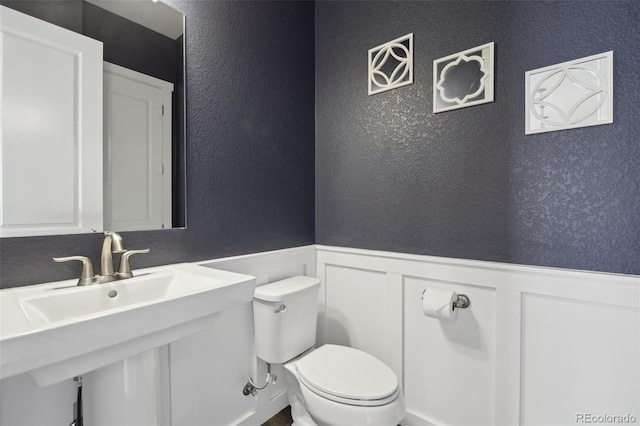 8803 Antero Ct, Arvada, CO 80007 - half bathroom featuring a textured wall, toilet, a wainscoted wall, a decorative wall, and a sink