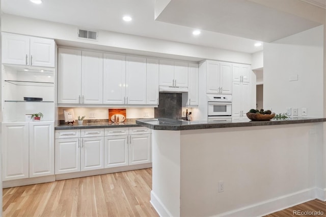 300 Hudson St Unit 109, Denver, CO 80220 - kitchen with under cabinet range hood, light wood finished floors, white cabinets, recessed lighting, and a peninsula