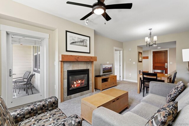 carpeted living room with a tiled fireplace and ceiling fan with notable chandelier