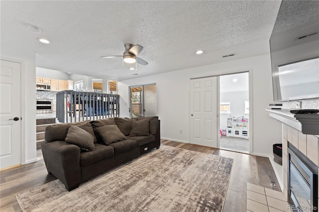 12119 Forest St, Thornton, CO 80241 - living room featuring a tile fireplace, ceiling fan, light wood-type flooring, recessed lighting, and a textured ceiling