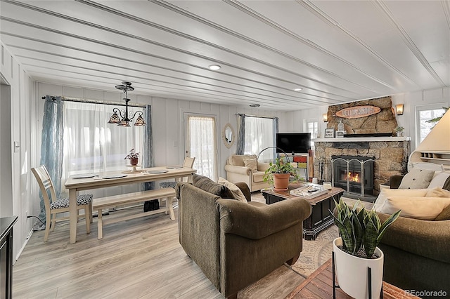 living area featuring light wood-style floors, an inviting chandelier, a wealth of natural light, and a stone fireplace