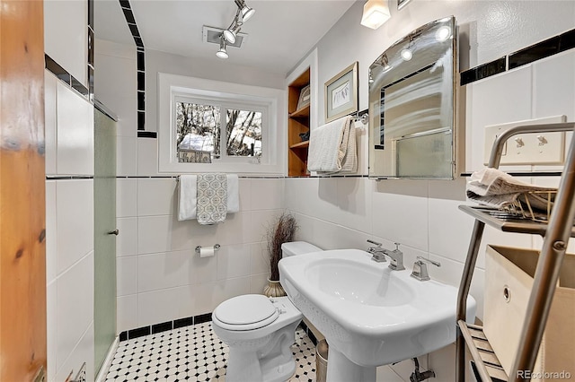 bathroom with tile patterned flooring, toilet, a sink, visible vents, and tile walls