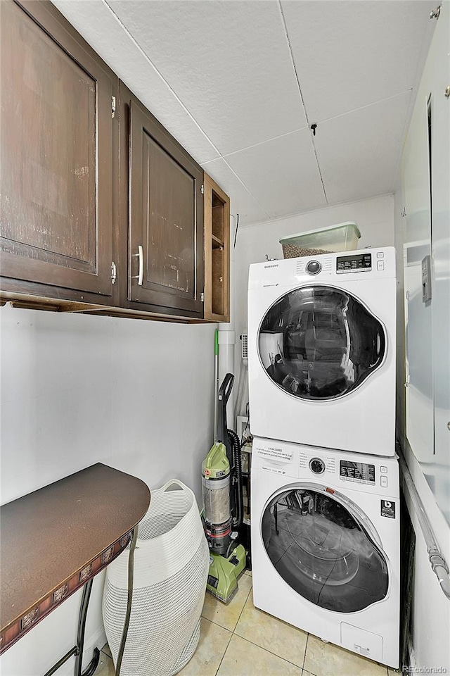 laundry area with cabinet space, stacked washer / drying machine, and light tile patterned flooring