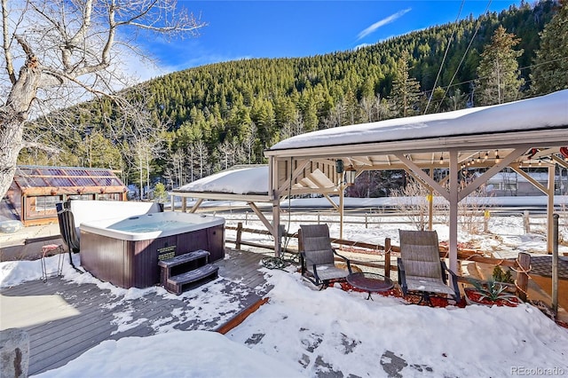 yard layered in snow with a hot tub, a deck, a wooded view, and a gazebo