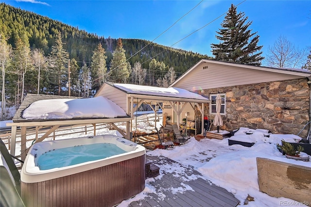 snow covered deck featuring a wooded view, a mountain view, and a hot tub