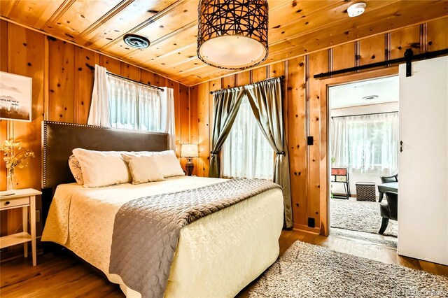 bedroom with visible vents, a barn door, wood walls, wood finished floors, and wooden ceiling