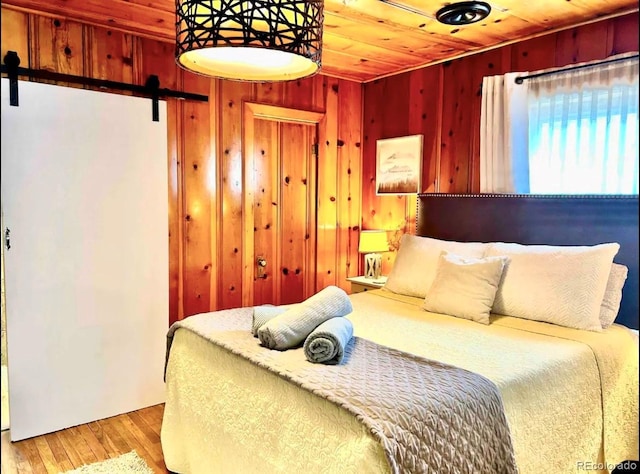 bedroom with light wood-style floors, wood ceiling, wood walls, and a barn door